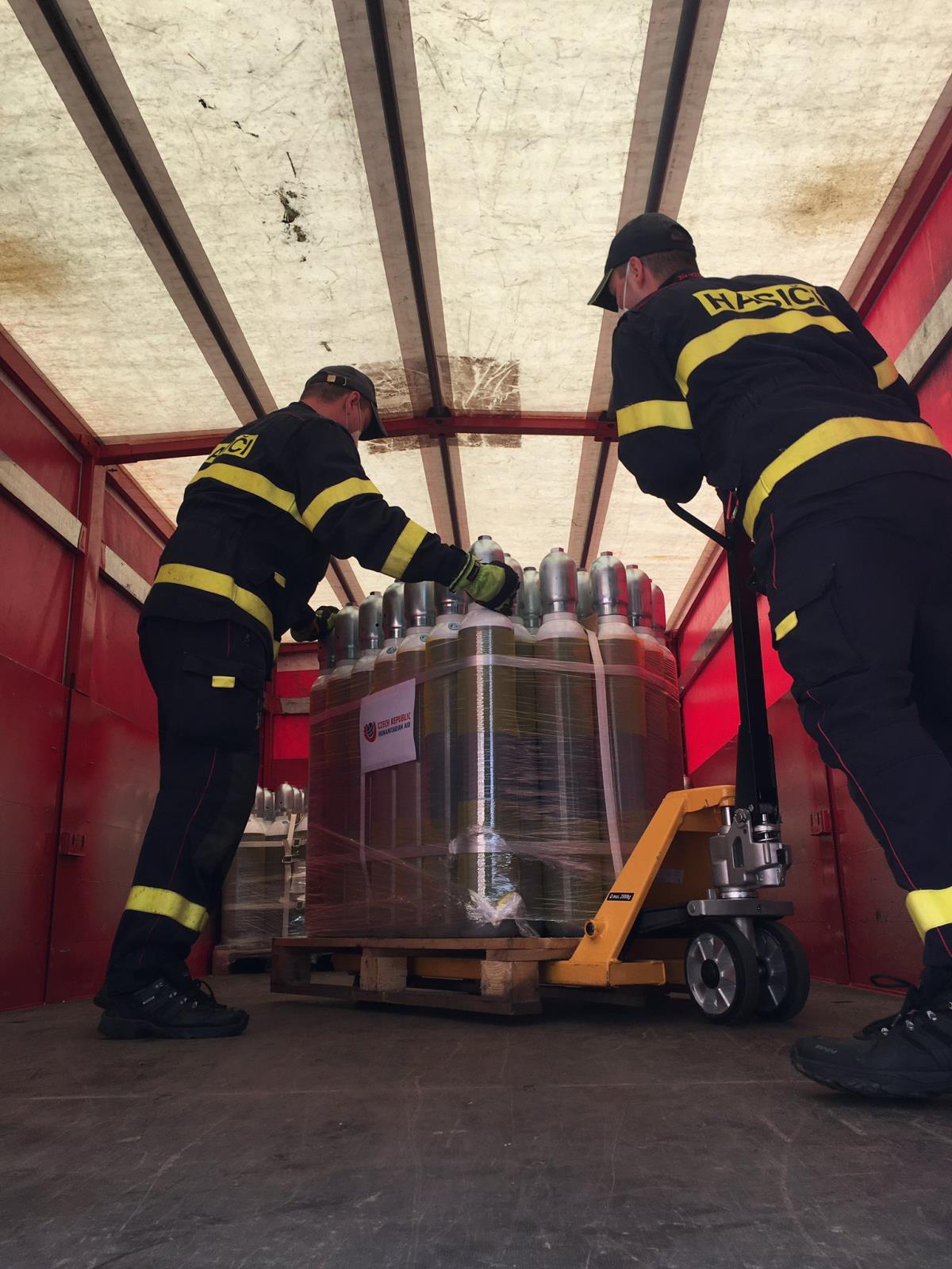 2 příslušníci HZS ČR nakládají nádoby s kyslíkem do nákladního vozu.JPG