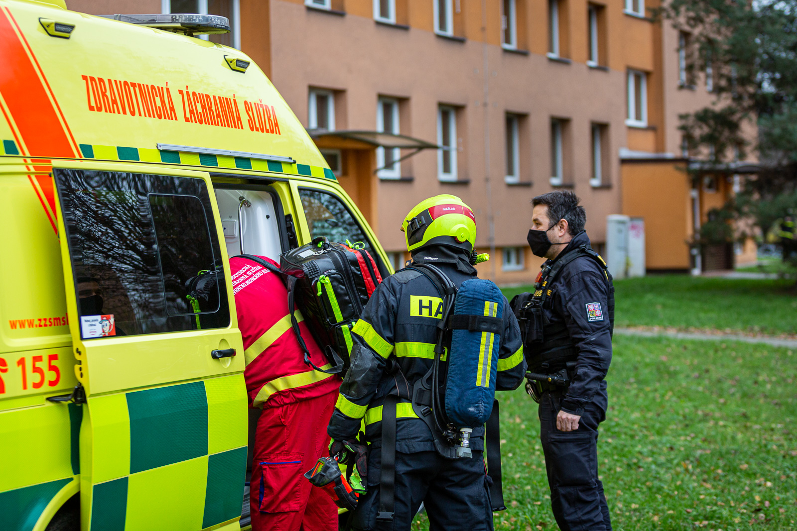 Hasič, policista a zdravotník stojí u vozu Zdravotnické záchranné služby, v jehož útrobách je jeden ze zraněných