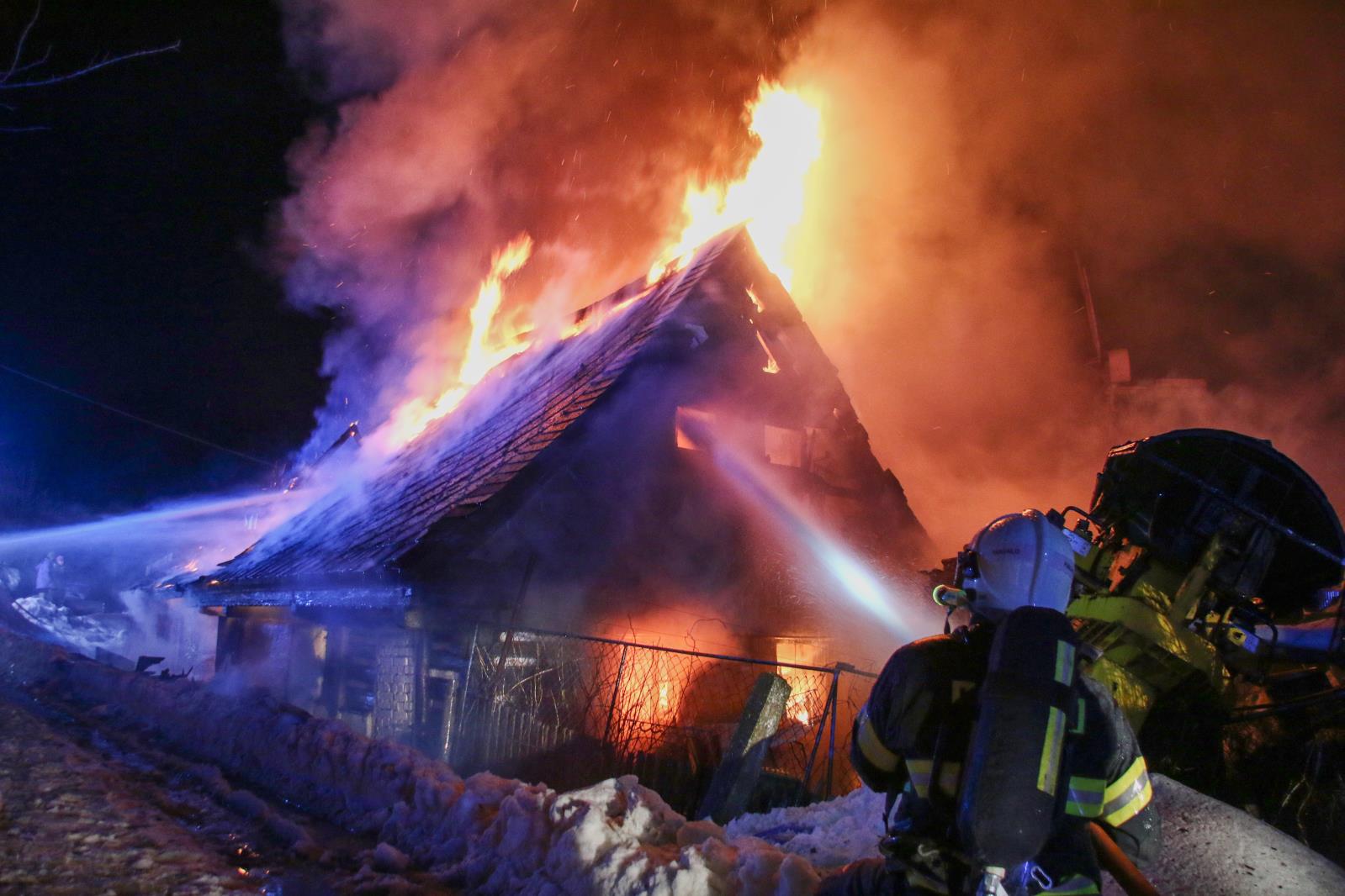 LIK_Požár domu v obci Plavy_hasič míří proud vody do okna hořícího objektu.jpg